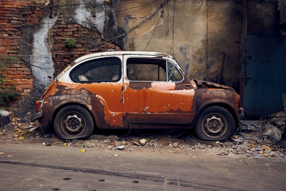A rusted car parked in front of a wall